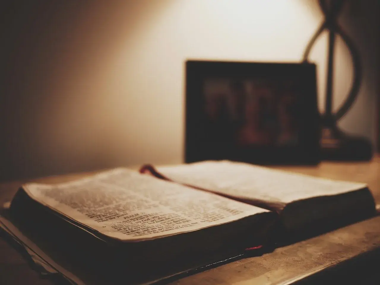 Otwarta Biblia na stole, obok ramka ze zdjęciem. Czy granie w lotto to grzech? Szukamy odpowiedzi w Piśmie Świętym.