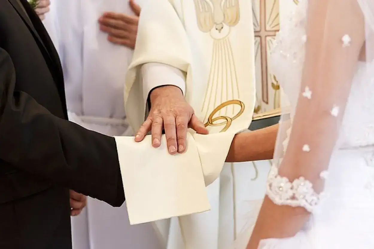 Odnowienie przysięgi małżeńskiej w kościele. Kapłan błogosławi parę, która trzyma się za ręce.