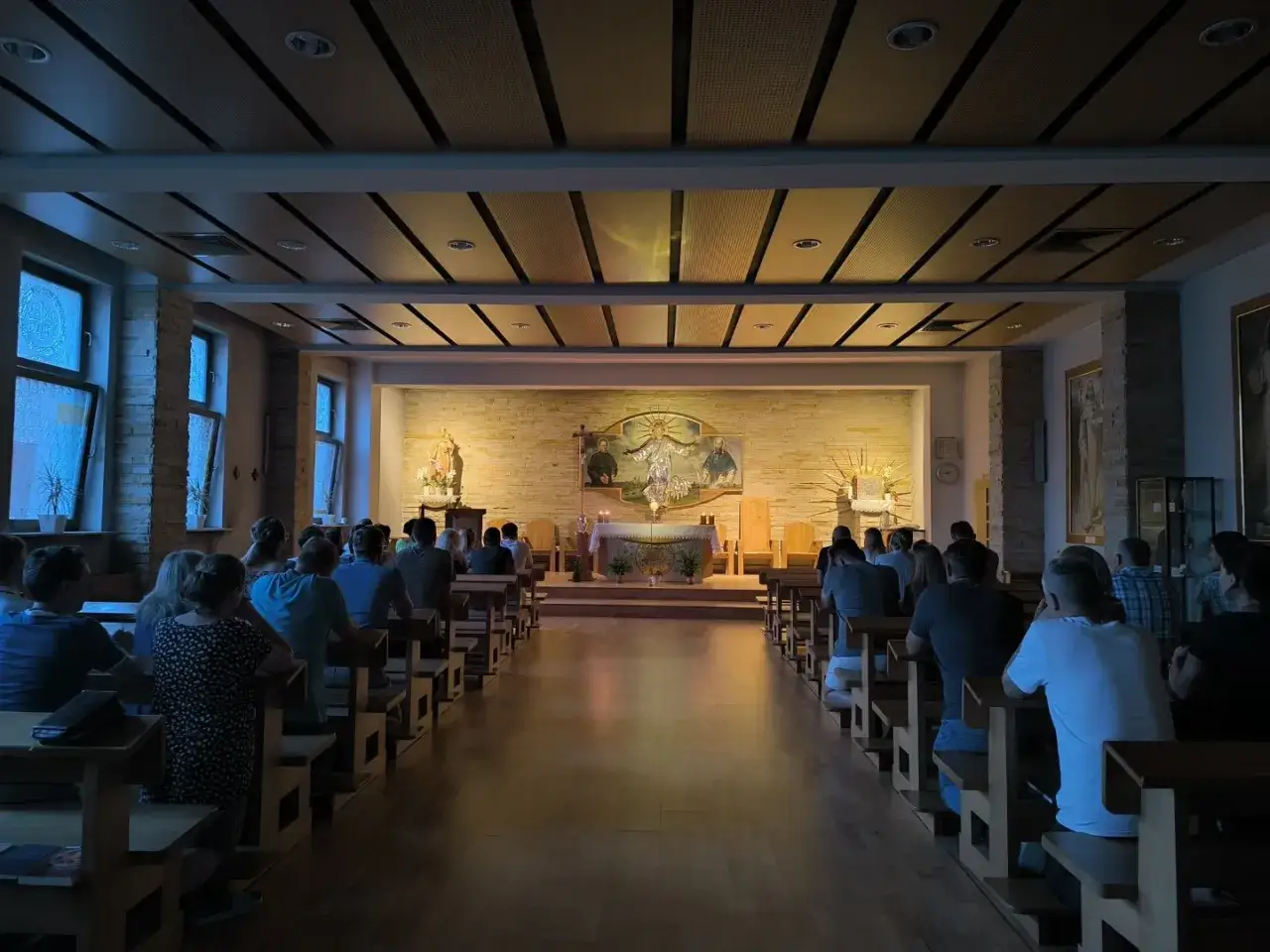 Ludzie siedzą w ławkach w kaplicy, przygotowując się do duchowego weekendu w pustelniach i domach rekolekcyjnych.