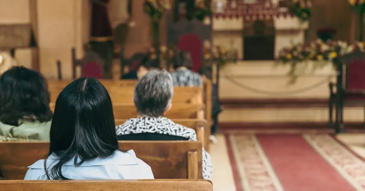 Ludzie siedzą w kościele, młoda kobieta z tyłu. Obraz symbolizuje dylematy pokoleniowe i przyczyny odejść młodych ludzi z kościoła.