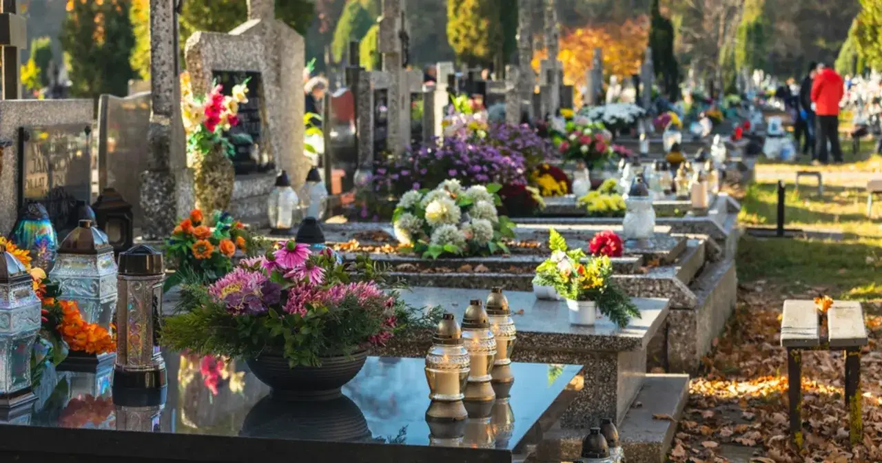 Skutki kradzieży na cmentarzach: jak zabezpieczyć wiązanki i znicze? Nagrobki ozdobione kwiatami i lampionami, jesienne liście.