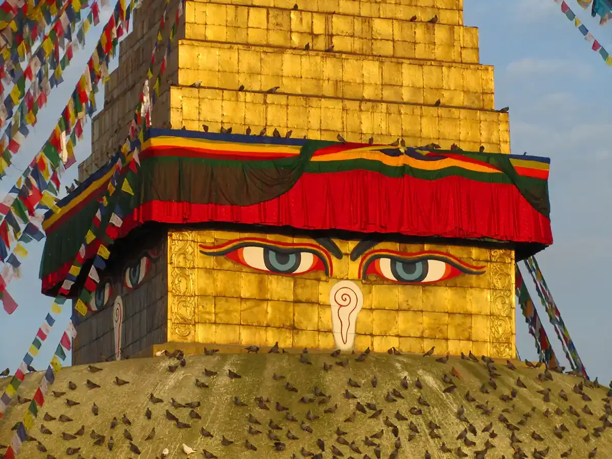 Złota stupa z oczami Buddy, ozdobiona kolorowymi flagami modlitewnymi. Warto odwiedzić takie miejsca święte w buddyzmie w Nepalu i Indiach.