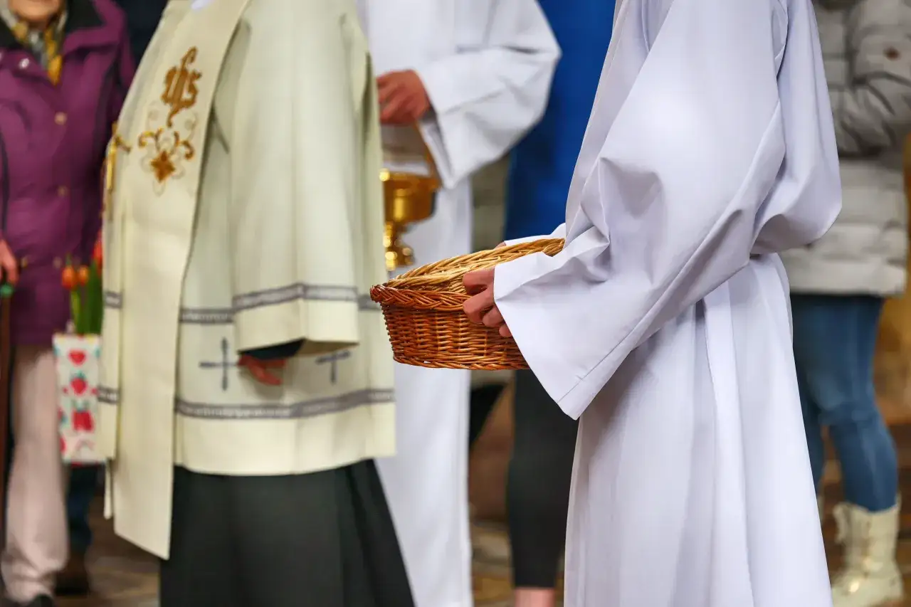 Dylematy pokoleniowe i przyczyny odejść młodych ludzi z kościoła. Osoby w strojach liturgicznych niosą koszyk.