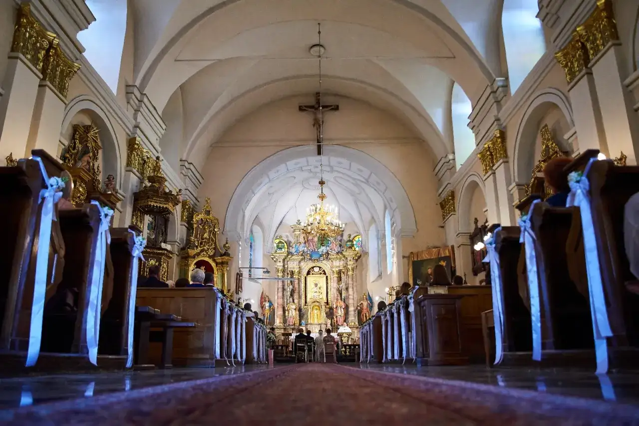 Wnętrze kościoła z ławkami ozdobionymi wstążkami. Widok na ołtarz i krucyfiks. Zmiana parafii zamieszkania może wpłynąć na formalności kościelne.