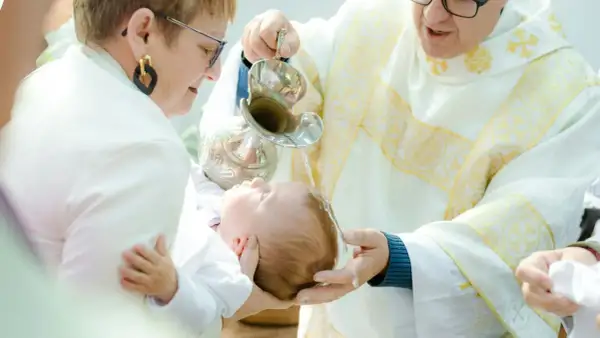 Chrzciny to wzruszająca uroczystość. Kapłan polewa wodą głowę dziecka, a rodzice trzymają je czule.