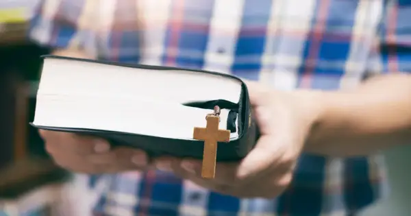 Osoba w kratę trzyma Biblię z drewnianym krzyżykiem, symbolizującym dwa przykazania miłości.