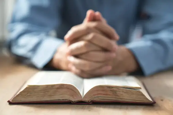 Modlące się dłonie nad otwartą Biblią. Warto zastanowić się, jak rozpoznać prawdziwe powołanie do kapłaństwa lub zakonu.