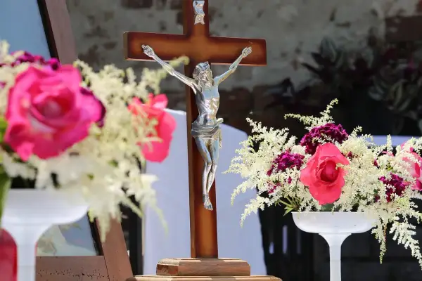 Drewniany krzyż z figurą Chrystusa, otoczony bukietami róż i białych kwiatów. Czy zdrada w myślach grzech?