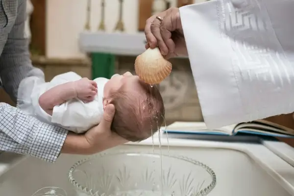 Chrzest dziecka. Kapłan polewa główkę wodą święconą z muszli. Poznaj wymogi i przyczyny braku zgody proboszcza na bycie chrzestnym.