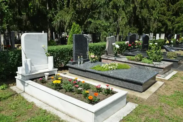 Zadbany grób z kwiatami i białym pomnikiem. Harmonogram prac, jak przygotować grób do Święta Zmarłych, obejmuje pielęgnację zieleni i porządkowanie.