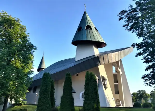 Nowoczesne sanktuarium z zielonymi dachami i krzyżem na szczycie, otoczone drzewami.