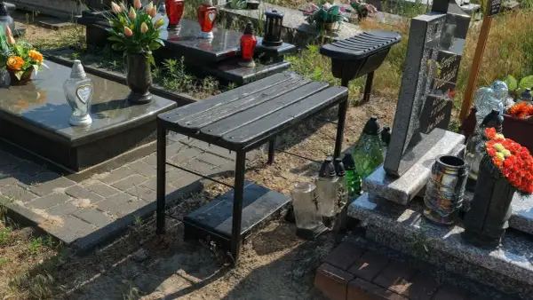 Ławeczka na cmentarzu – czy na cmentarzu można postawić ławeczkę? Wymogi i zgody. Obok nagrobków i zniczy stoi czarna ławka.