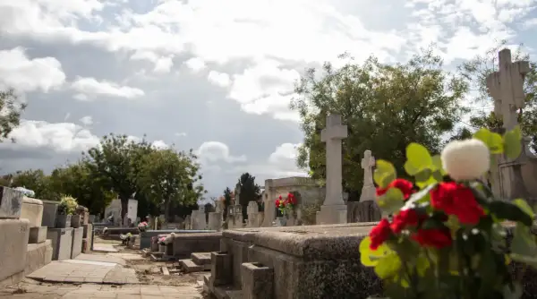 Nagrobek z krzyżami i kwiatami na tle pochmurnego nieba.